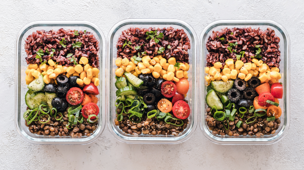 Three glass lock containers containing the same meal of brown rice, corn, cucumber slices, black olives, cherry tomatoes, green onion, and lentils.